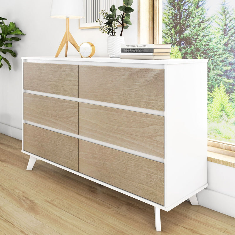 Modern white and natural wood six-drawer dresser in a minimalist bedroom, styled with a wooden tripod lamp, gold clock, white ceramic vase with greenery and stacked books beside a sunny window on hardwood floors