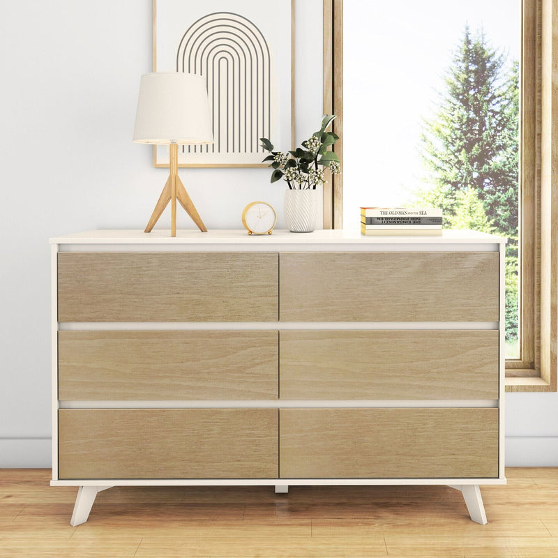 Mid-century modern wooden six-drawer dresser in bright Scandinavian bedroom with tripod table lamp, potted greenery, gold clock and stacked books by a sunlit window