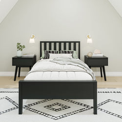 Modern bedroom interior with black bed frame, patterned blanket, and matching bedside tables on a geometric rug.