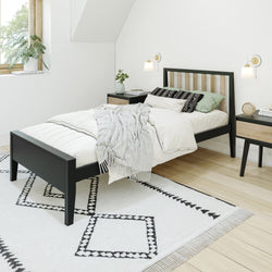 Cozy modern bedroom with Scandinavian design featuring a black frame bed, patterned rug, and minimalist decor.