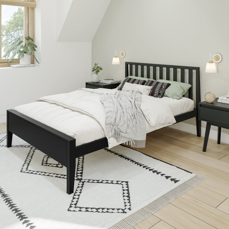 Minimalist Scandinavian bedroom with black wooden slatted bed frame, white duvet and textured throw, geometric black-and-white area rug, matching black nightstands with wall sconces, hardwood floors and potted plant by sunlit window