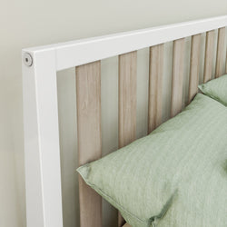 Wooden bed frame with white accents and green cushions in modern bedroom setting.