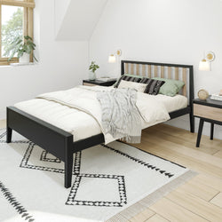 Modern bedroom interior with a black wooden bed frame, white bedding, green pillows, and geometric rug.