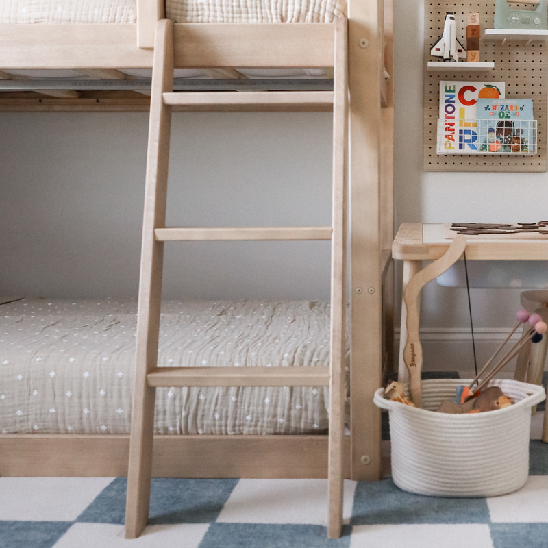 Neutral kids bedroom with natural wood loft bed ladder, patterned rug, woven toy basket and pegboard book storage