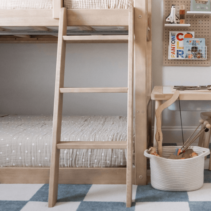 Minimalist kids bedroom with natural wood bunk bed ladder, neutral quilted bedding, woven toy storage basket and wooden desk with pegboard
