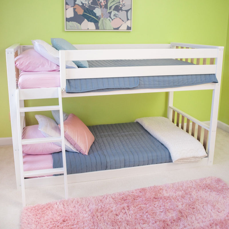 White wooden twin bunk bed in a children's bedroom with pink and blue bedding, ladder, green accent wall and plush pink rug
