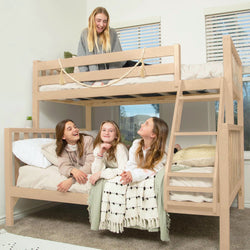 Four smiling girls enjoying a beige wooden twin-over-twin bunk bed with ladder, cozy blankets and pillows in a bright kids' bedroom — ideal kids' bedroom furniture and sleepover setup
