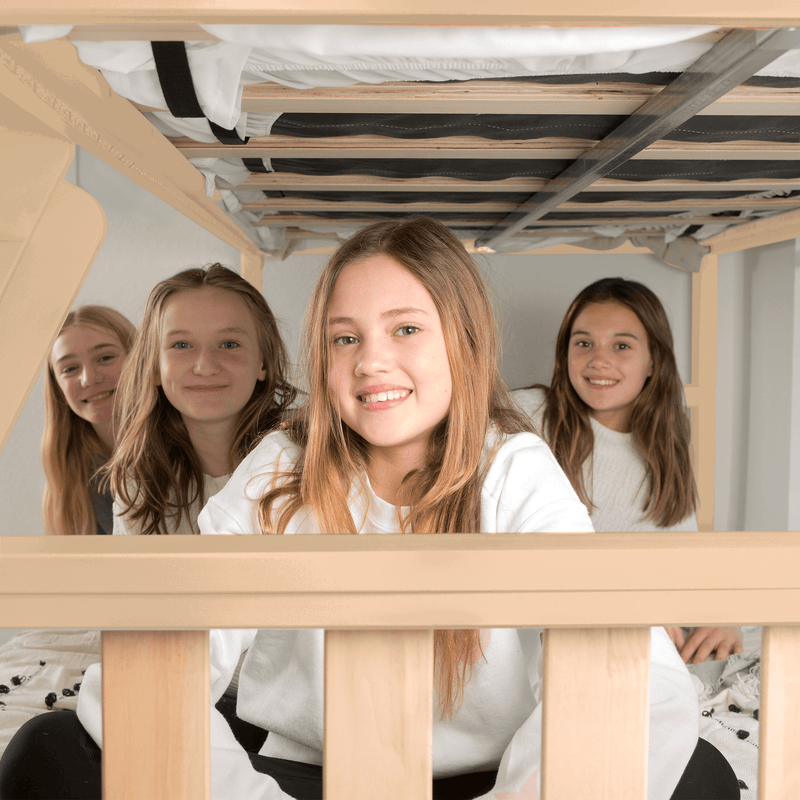 Smiling teenage girls friends gathered under a wooden bunk bed in a cozy bedroom sleepover portrait with natural light and casual decor