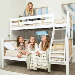 White wooden twin-over-full bunk bed with ladder in bright kids bedroom, four smiling girls on neutral bedding, modern farmhouse style
