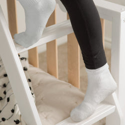Child's white socks stepping on a white wooden learning tower step stool in a neutral nursery — Montessori toddler step stool and nursery safety