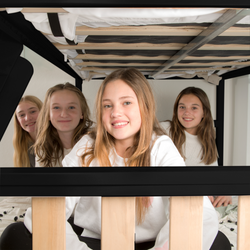Four smiling girls playing under a bunk bed during a sleepover in a bright, cozy bedroom