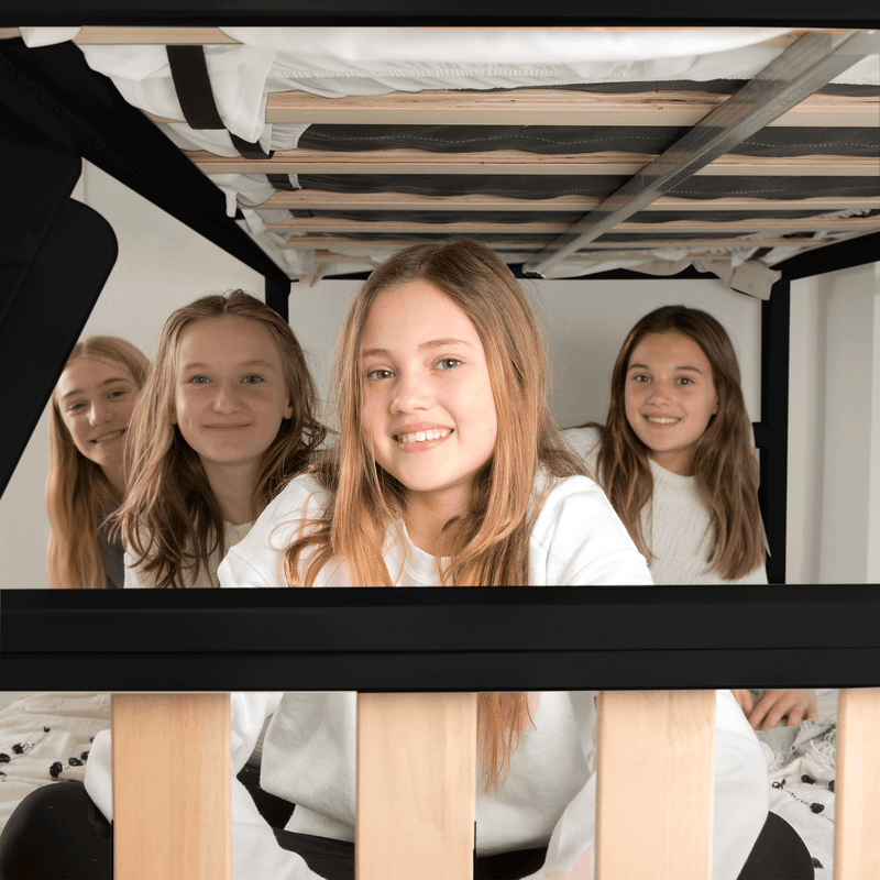 Four smiling teen girls sitting together under a bunk bed for a sleepover in a cozy kids' room