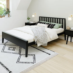 Modern minimalist bedroom with black bed frame, white bedding, geometric rug, and wall-mounted lamps.