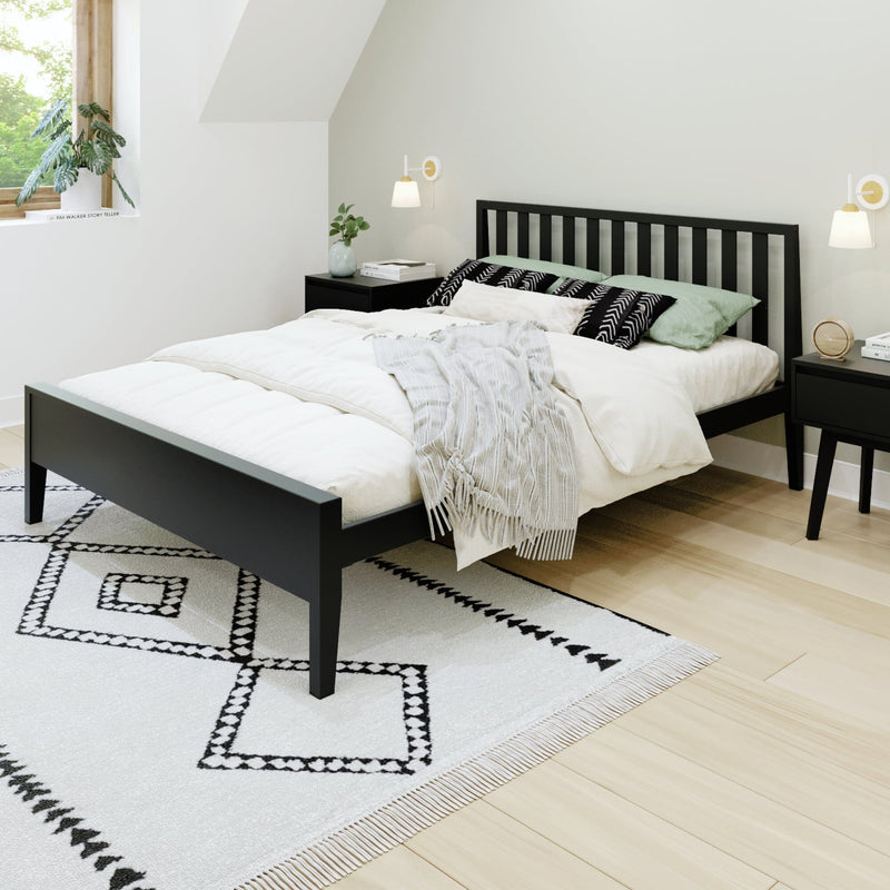 Modern minimalist bedroom with black slatted bed, white bedding, green accent pillows, geometric rug and wood nightstand