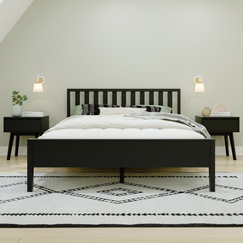Minimalist modern bedroom with black slatted bed frame, white bedding and pillows, matching black nightstands, wall sconces, potted plant and geometric black-and-white rug
