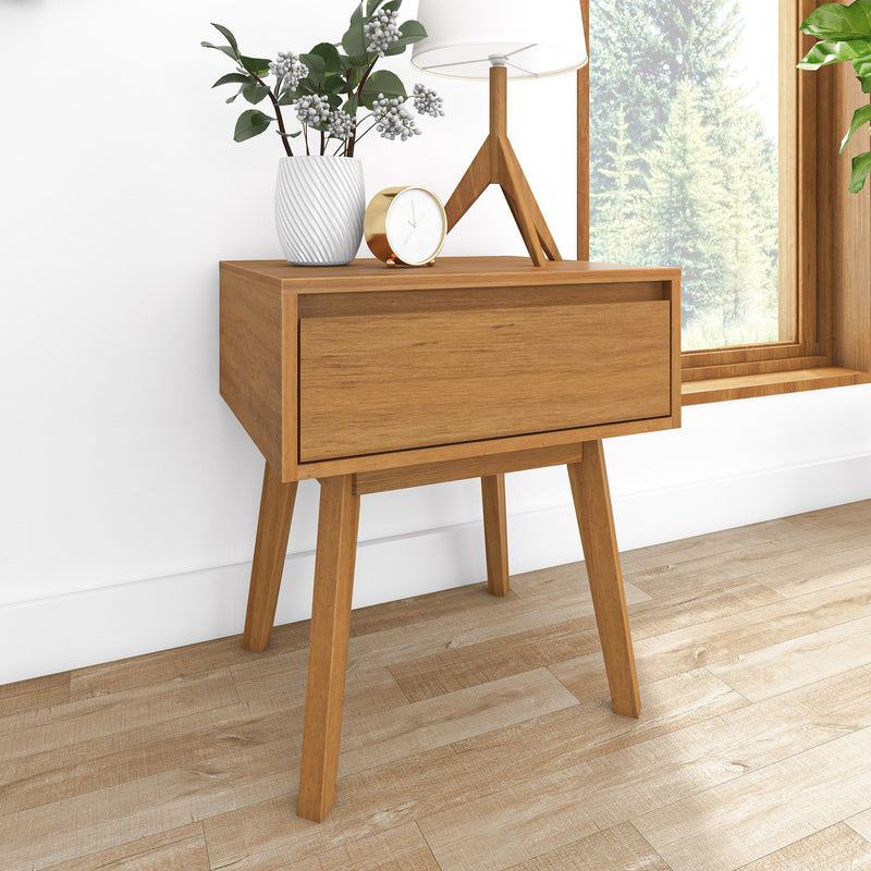 Mid-century modern wooden nightstand styled for bedroom decor with white ceramic vase, gold alarm clock, tripod lamp and pine forest window view