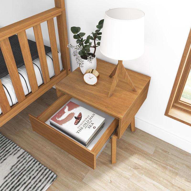 Modern wooden nightstand and bed frame with a white tripod table lamp, gold alarm clock, potted eucalyptus plant, and drawer showing the book "The Old Man and the Sea" — minimalist bedroom decor