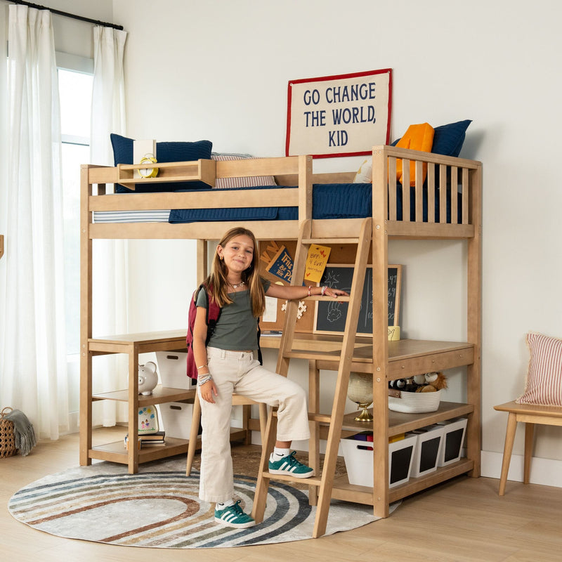 Young girl standing by natural wood loft bed with ladder, built-in desk and storage in modern kids' bedroom, navy bedding and "Go change the world, kid" wall banner