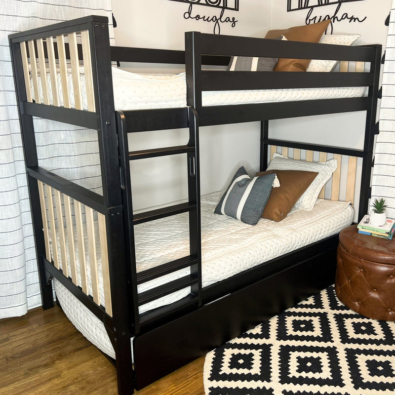 Black wooden twin-over-twin bunk bed with built-in ladder, natural wood slats, under-bed drawer, white quilted mattresses and decorative pillows in modern kids' bedroom