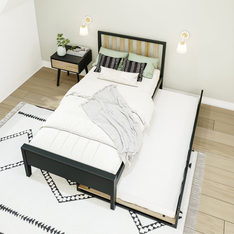 Modern minimalist bedroom interior with black metal bed frame and pull-out trundle, light wood slat headboard, neutral linens, patterned black-and-white rug, nightstand with plant, wall sconces and hardwood floor