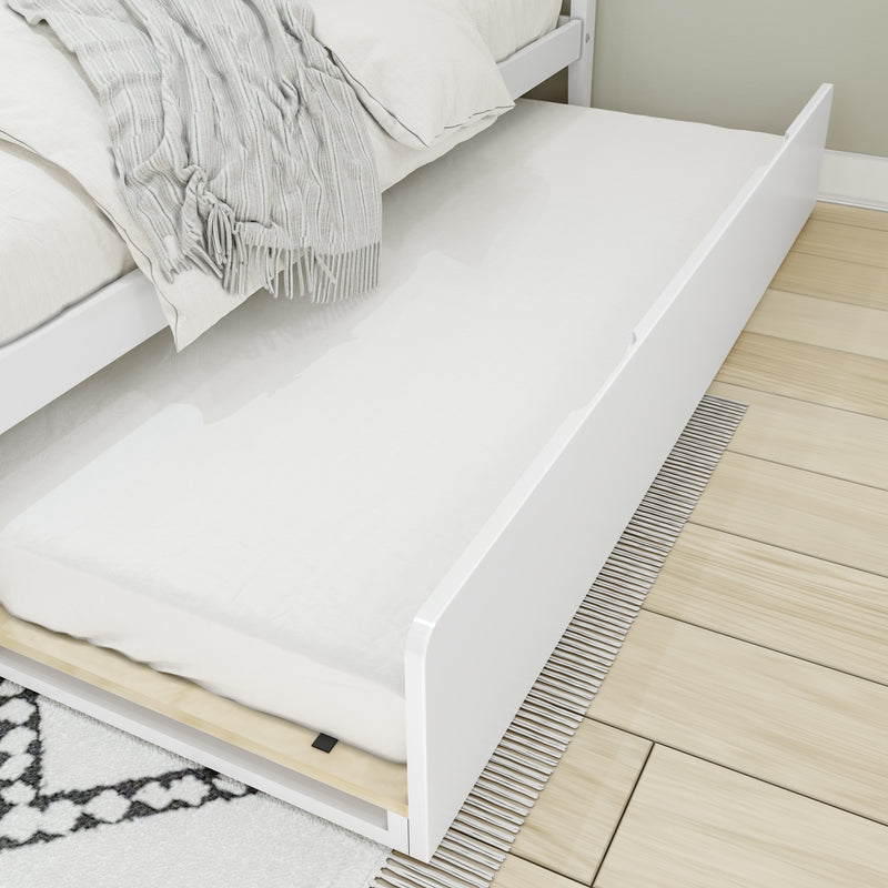 White pull-out trundle bed with mattress and light gray fringed throw tucked under a white platform bed on light hardwood floor