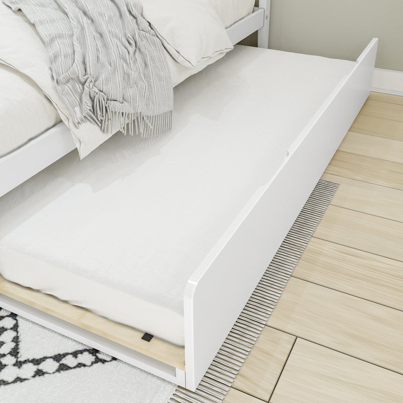 White pull-out trundle bed with mattress and light gray fringed throw tucked under a white platform bed on light hardwood floor
