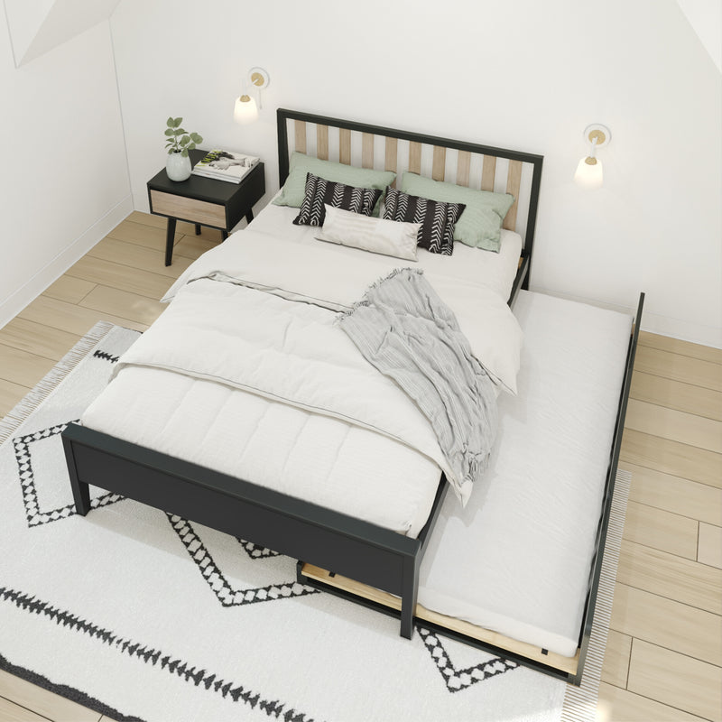 Modern Scandinavian bedroom featuring a black wood trundle bed with white bedding and a gray throw, green and patterned accent pillows, wood-and-black nightstand with plant and magazines, wall-mounted sconces and geometric rug on light hardwood floor.