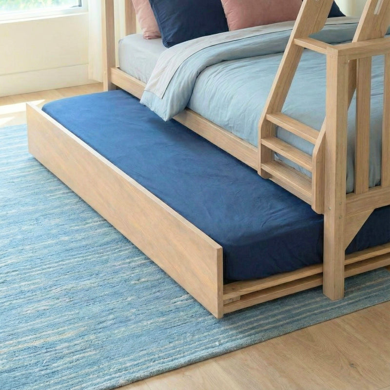 Light oak wooden trundle bunk bed with ladder in kids bedroom, navy and pastel blue bedding and blue area rug on hardwood floor