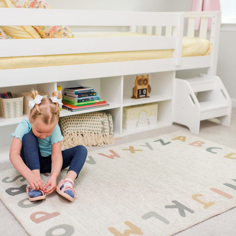 Child tying pink sandals on alphabet rug in a bright kids' bedroom under a white loft bed with built-in storage, bookshelf and toys