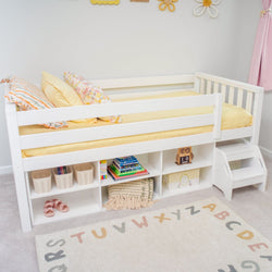 Kids' white loft bed with built-in storage shelves, yellow bedding, and colorful decorative pillows in a bright nursery room.