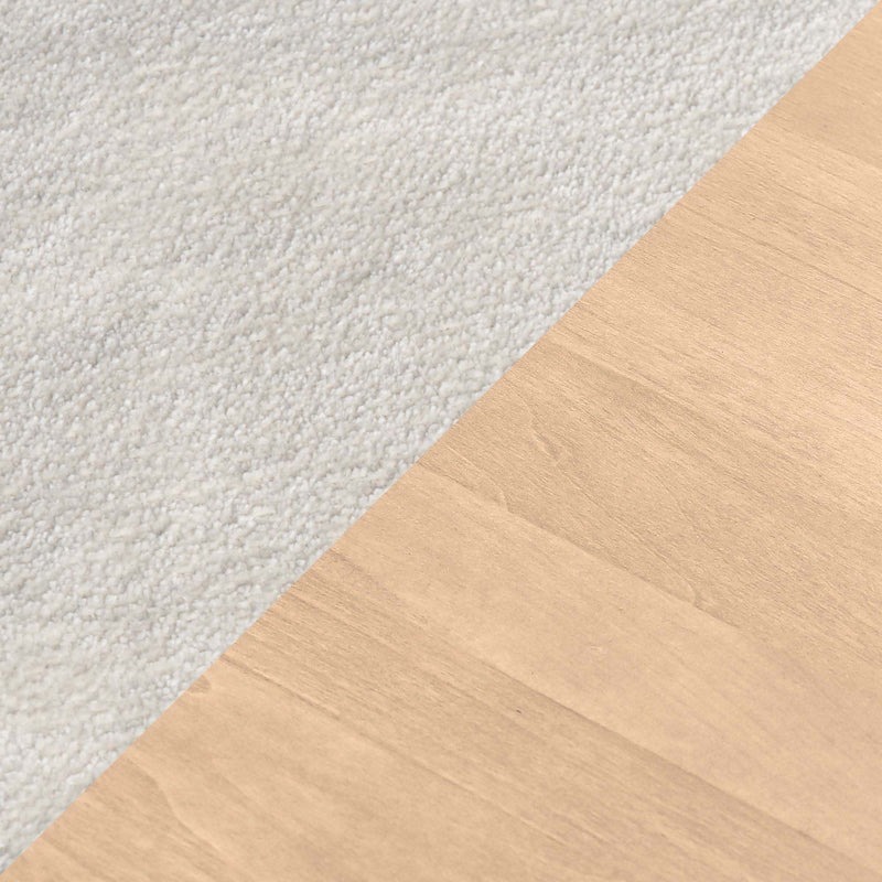 Close-up diagonal carpet-to-hardwood transition: plush white carpet to light oak hardwood flooring showing carpet texture and wood grain.