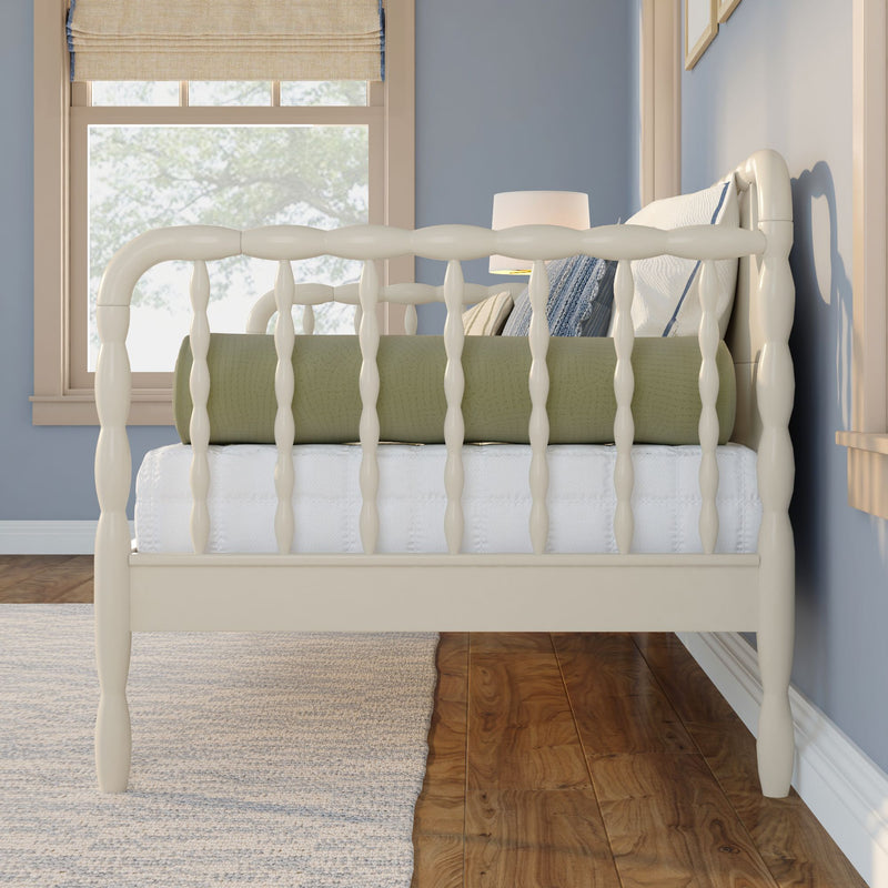 Cream spindle bed frame in a coastal blue bedroom with green quilt, textured pillows, bedside lamp and hardwood floor natural light