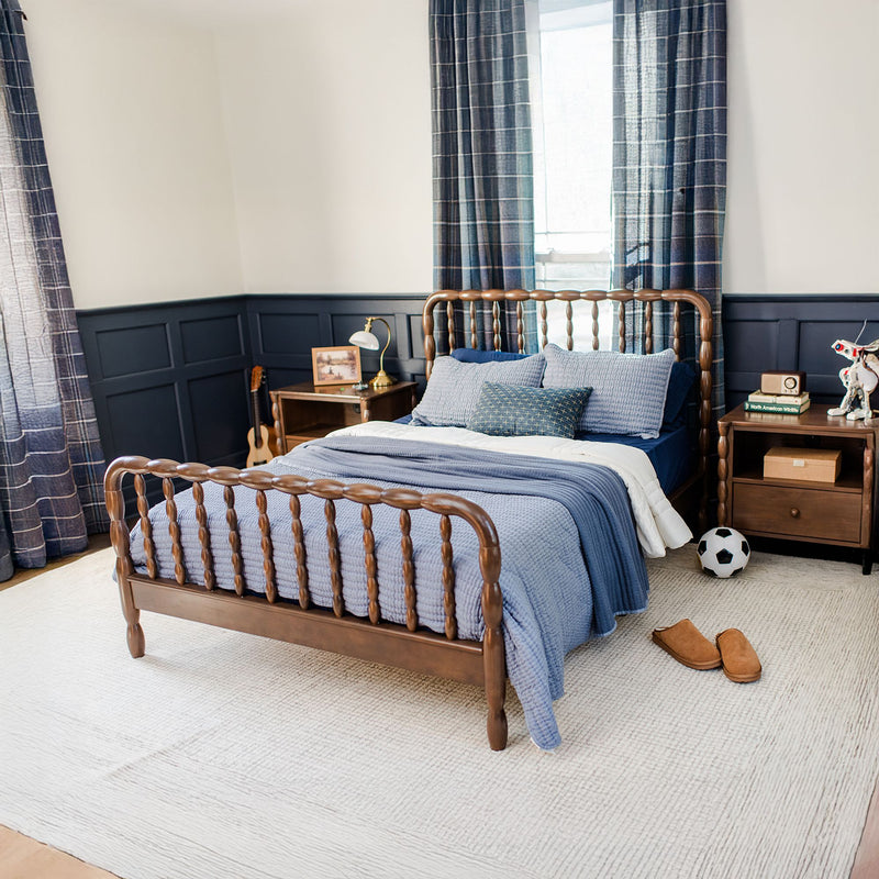 Cozy navy-and-wood kids' bedroom featuring a spindle wooden bed frame with blue quilted bedding, navy wainscoting, plaid curtains, wooden nightstands with lamp, soccer ball, slippers, rug and ukulele