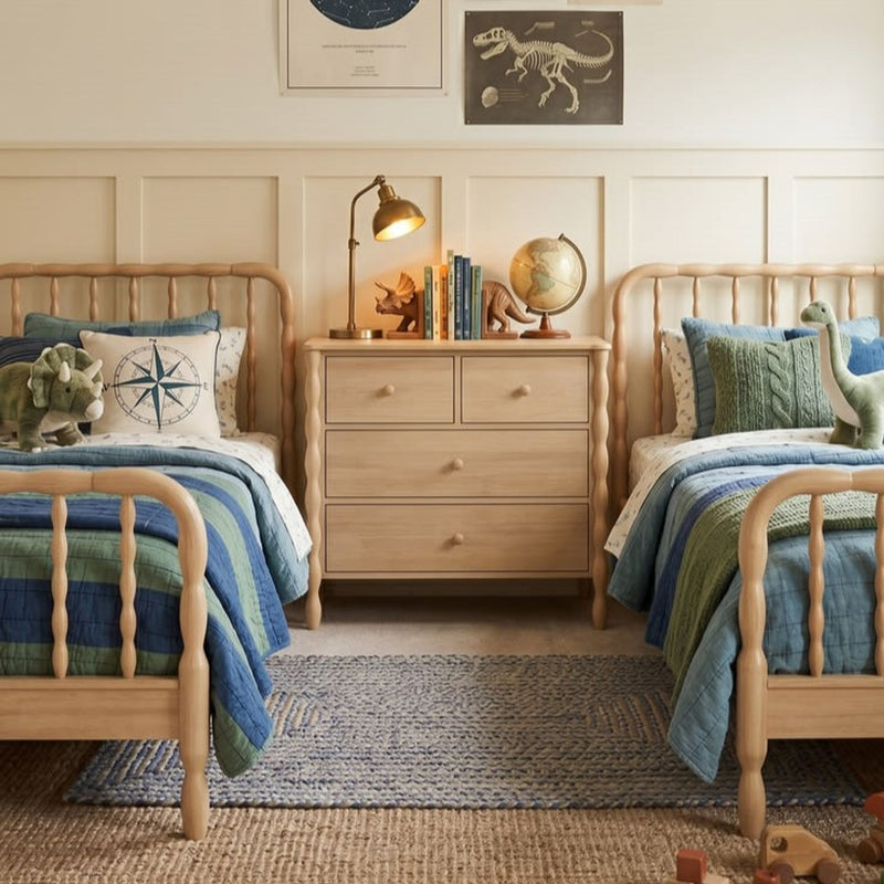 Kids twin bedroom with light wooden spindle beds, blue-green quilts, bedside dresser with brass lamp and globe, nautical compass pillow and dinosaur toys