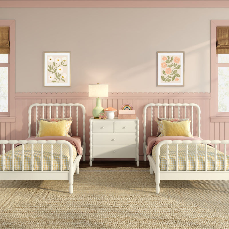Pastel pink twin girls bedroom nursery with white spindle twin beds, yellow gingham bedding, white nightstand and lamp, scalloped wainscoting and floral wall art