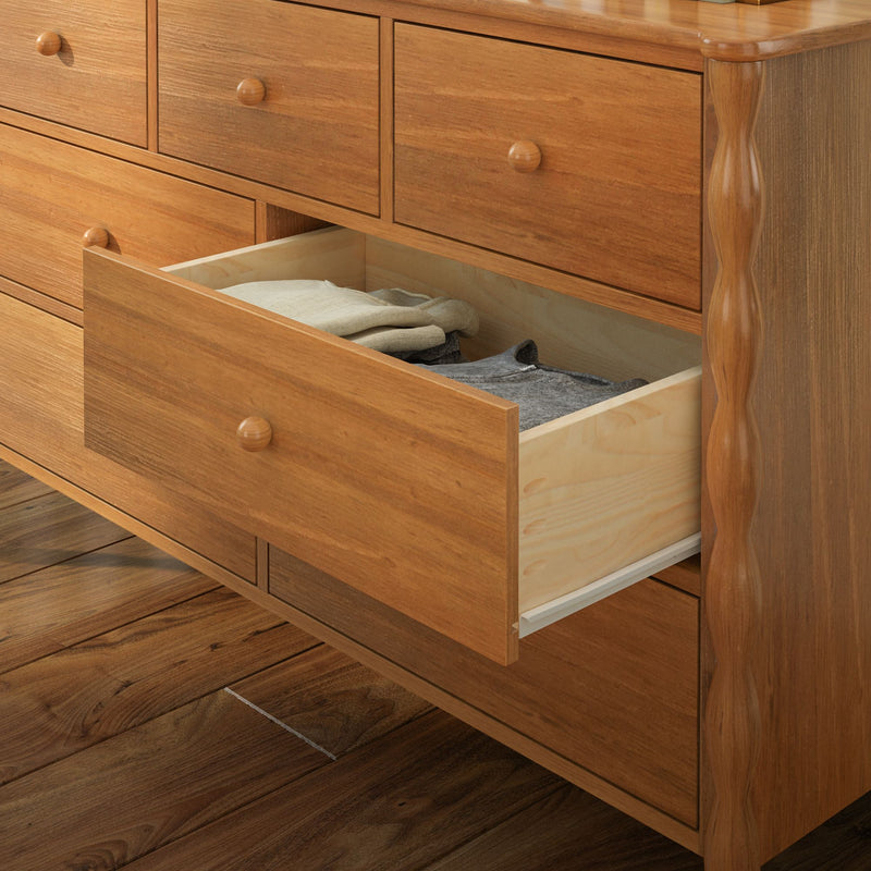 Solid wood dresser with open drawer revealing folded clothes, natural oak finish and round wooden knobs on hardwood bedroom floor, bedroom storage furniture
