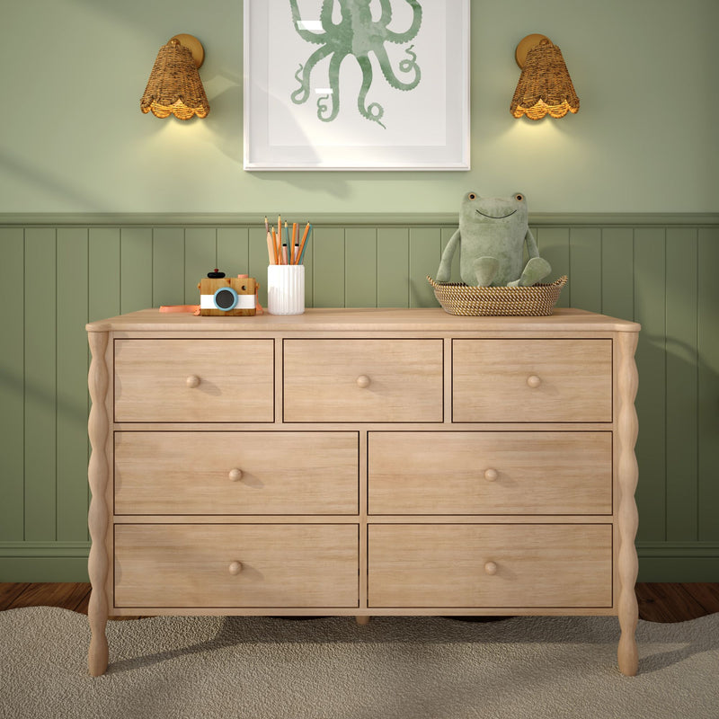 Light wood kids dresser in green paneled nursery with plush frog in woven basket, wooden toy camera, pencil cup, octopus wall art and rattan wall sconces, modern nursery decor