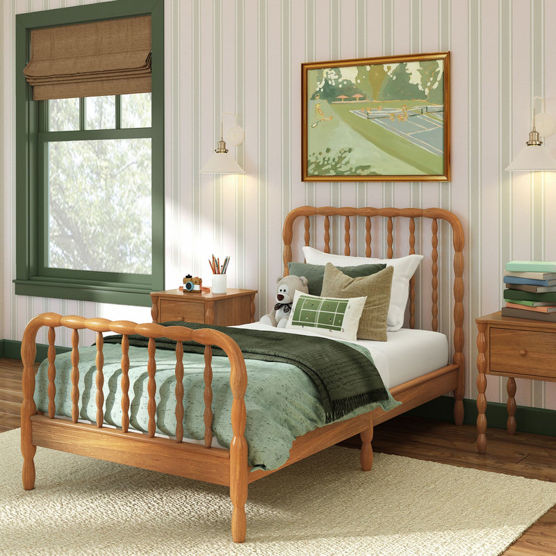 Cozy kids bedroom with wooden spindle bed, green bedding, teddy bear, striped wallpaper, framed artwork and bedside table with lamp