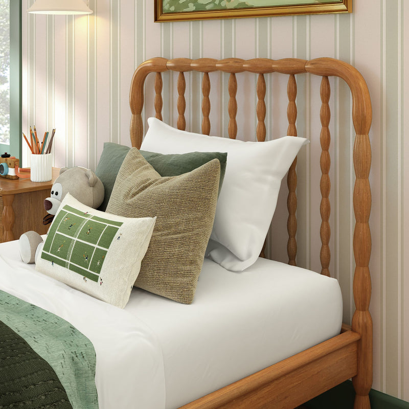 Cozy children's bedroom corner with wooden spindle bedframe, green and beige pillows, teddy bear, striped wallpaper, bedside table and lamp