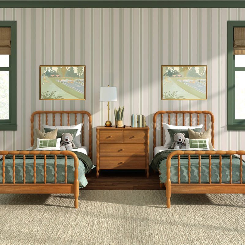 Kids' bedroom with two twin wooden spindle beds, green bedding and teddy bears, central wooden dresser with lamp, striped wallpaper, framed artwork and sunlit windows, cozy children's interior design