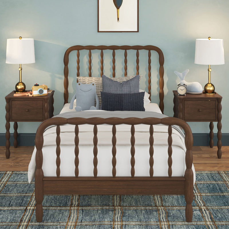Children's bedroom with wooden spindle bed, blue accent wall, matching bedside tables and brass table lamps, plush toys, alarm clock and decorative pillows