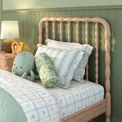 Coastal-inspired kids bedroom with wooden spindle headboard, mint-green striped and patterned bedding, round bolster pillow, plush octopus toy and wicker lamp on a wooden nightstand