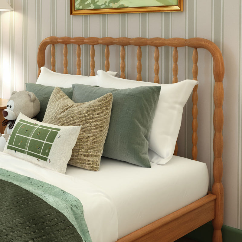 Cozy bedroom with wooden spindle headboard, white sheets and green quilted bedding, layered green and textured accent pillows, sports-themed lumbar pillow and plush teddy bear—stylish bedroom decor