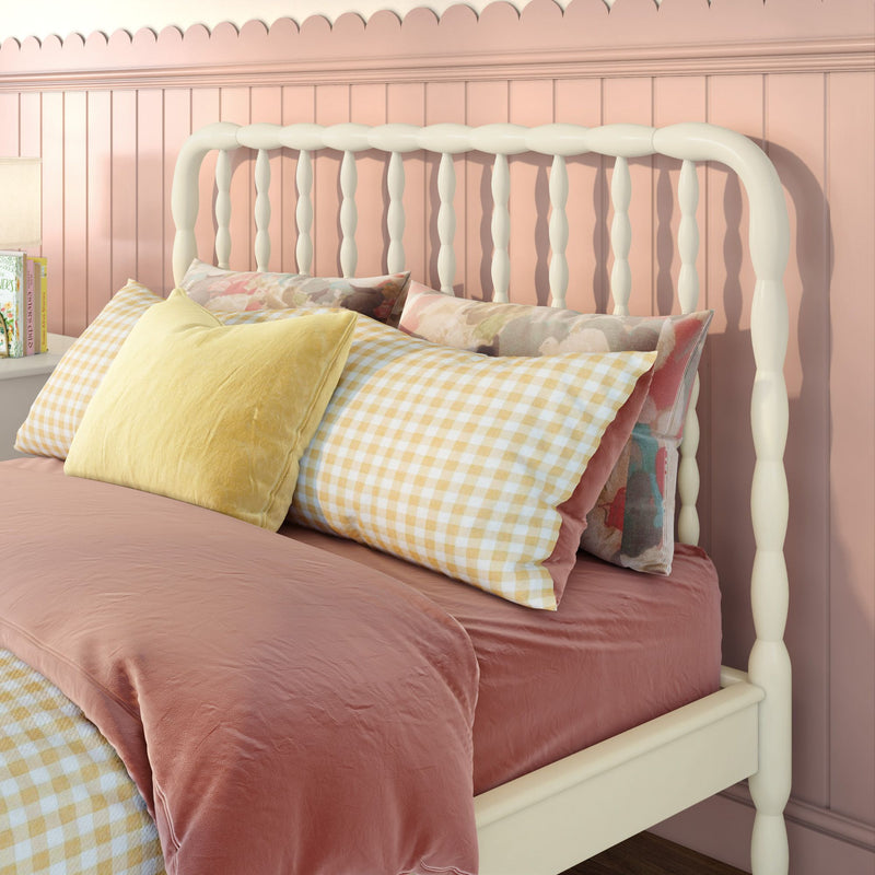 Pink bedroom with white spindle headboard, blush duvet, yellow gingham pillow and floral throw pillows