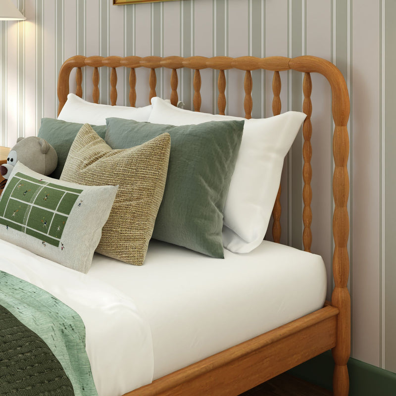 Close-up of a wooden spindle headboard with white bedding, green and woven decorative pillows, a plush toy and pale green vertical striped wallpaper, cozy bedroom decor