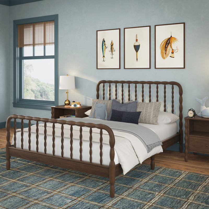 Cozy coastal bedroom with wooden spindle bed, seafoam-blue walls, layered neutral bedding and pillows, plaid blue area rug, nightstand with lamp and alarm clock, and three framed nautical prints above the headboard