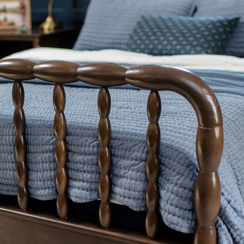 Close-up of a wooden spindle bed frame with blue textured quilt and geometric patterned pillows, cozy bedroom decor