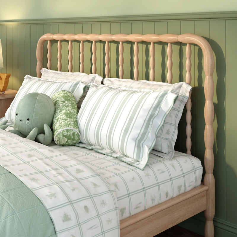 Natural wood spindle headboard against sage green beadboard wall with light green striped bedding and plush octopus pillow in cozy cottage bedroom