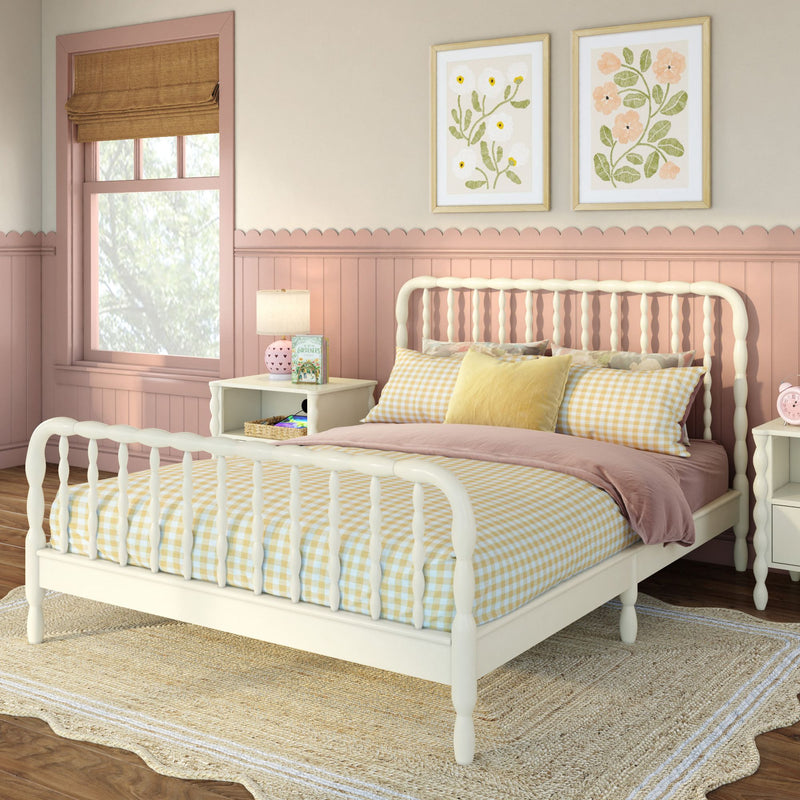 Pastel pink girls bedroom with cream spindle bed, yellow gingham bedding, scalloped wainscoting, framed floral prints, woven jute rug and Roman shade