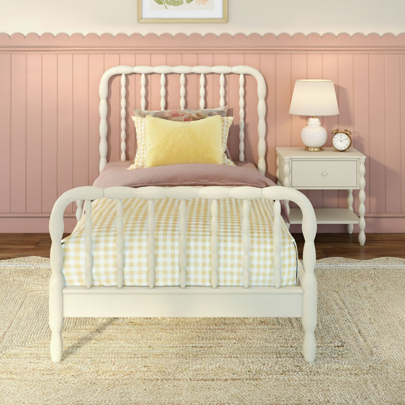 Pastel pink children's bedroom with white spindle bed, yellow gingham bedding and pillow, scalloped wainscoting and bedside table with lamp and alarm clock